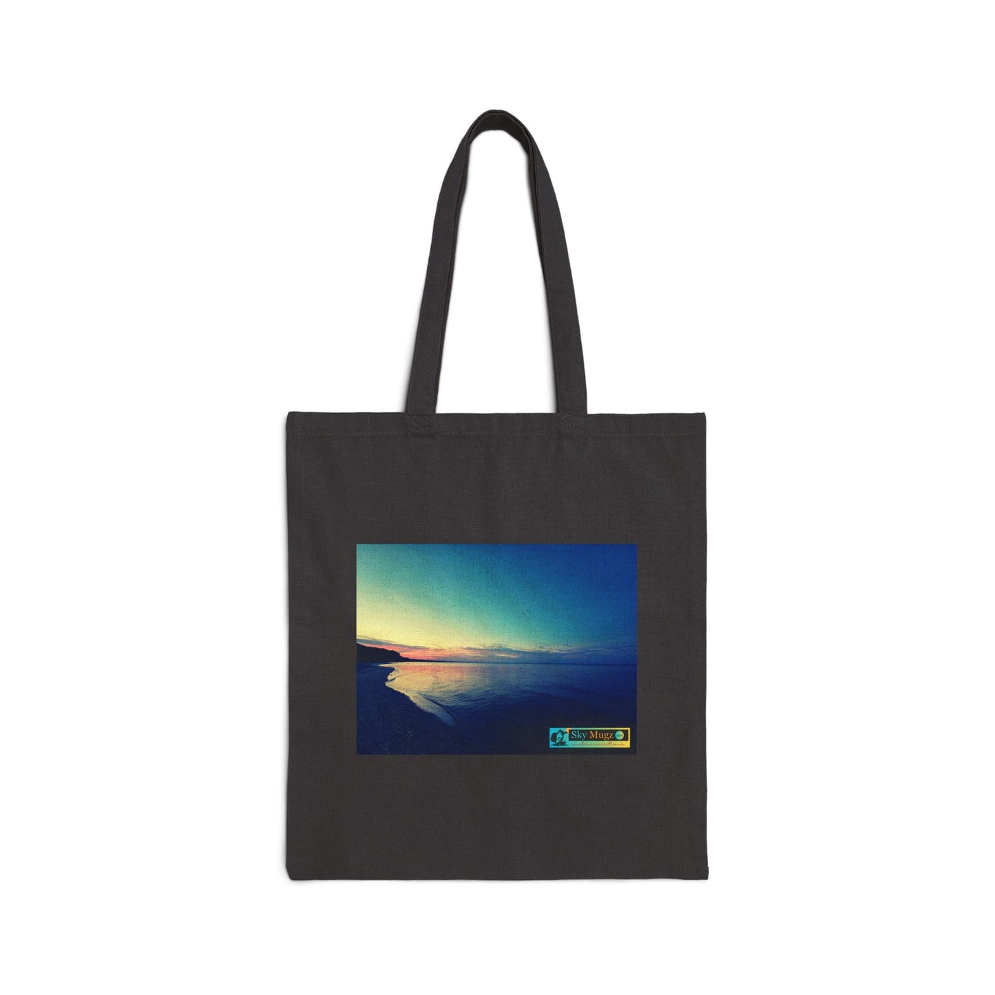 A dark charcoal gray canvas tote bag with black shoulder straps, featuring a square graphic print of a scenic sunset over water on the front. The print has a small colorful logo in the bottom right corner that reads 'The Color of Time'.